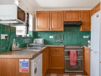 a kitchen with wooden cabinets and green tiles at Dairy Cottage - Uk49834 in Lanivet