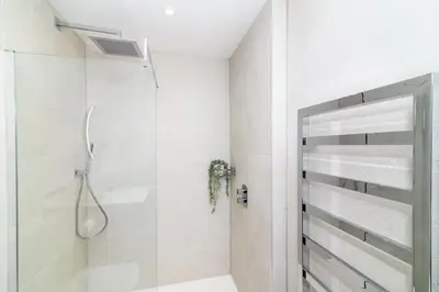 a white bathroom with a shower and a glass door at Luxury Apartment very close to Tolcarne Beach in Newquay