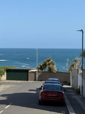 a red car parked on a road near the ocean at Seaweed Suite, secluded seaside stay with garden view in Newquay