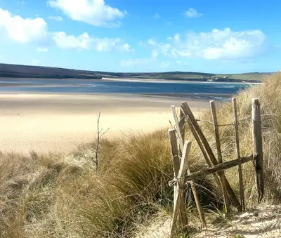 a wooden fence in the sand near a body of water at Riverwood Lodge, Padstow in Padstow