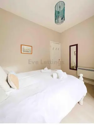 a white bed in a bedroom with a chandelier at Mermaid Apartment, A Colourful Coastal Escape By The Sea, Child Friendly in St Ives