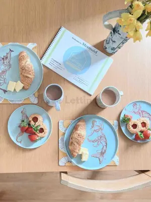 a table with plates of food and a book at Mermaid Apartment, A Colourful Coastal Escape By The Sea, Child Friendly in St Ives