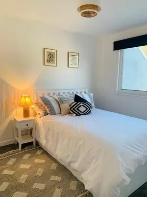 a white bed in a bedroom with a lamp at Lovely two bed flat with a sea view next to beach in Porthtowan