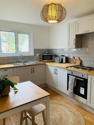 a kitchen with white cabinets and a table at Lovely two bed flat with a sea view next to beach in Porthtowan