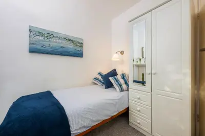 a white bedroom with a bed and a cabinet at Penstraze cottage near Gylly Beach in Falmouth