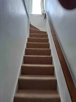 a stairway with brown carpeted stairs and a window at Penstraze cottage near Gylly Beach in Falmouth