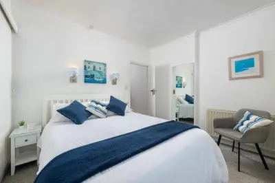 a white bedroom with a bed and a chair at Penstraze cottage near Gylly Beach in Falmouth