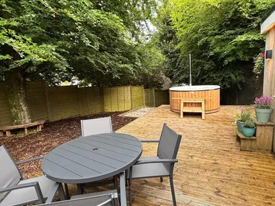 a patio with a table and chairs and a tub at Cornish wooden cabin & wood fired hot tub in Gwennap