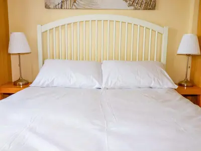 a bed with white sheets and two lamps on tables at H2 Atlantic Bay Holiday Park in Padstow