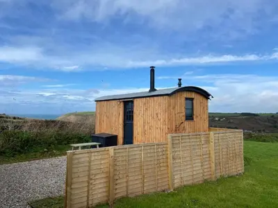 a small wooden building with a fence in the grass at Travellers Rest Glamping Pods & Shepherds Hut in Newquay