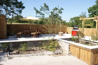 a backyard with a table and an umbrella and a grill at Lower Mulberry Cottage in Bodmin