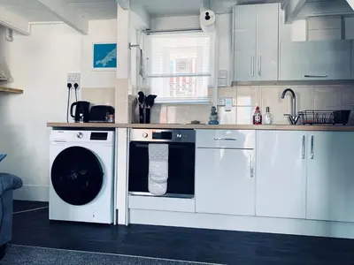 a kitchen with white cabinets and a washing machine at Holm Cottage near Charlestown in St Austell