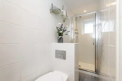 a white bathroom with a toilet and a vase of flowers at Dolls Cottage in Looe