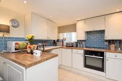a kitchen with white cabinets and blue tiles at Dolls Cottage in Looe