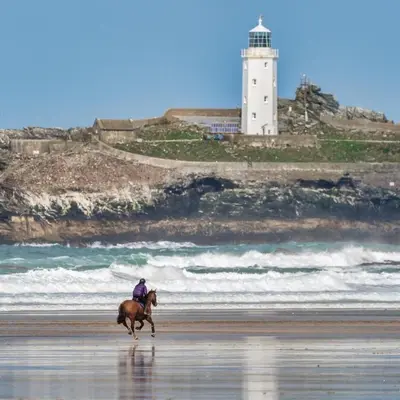 a person riding a horse on the beach with a lighthouse at Morthana Shepherd Hut in Scorrier