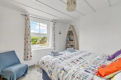 a bedroom with a bed and a chair and a window at Finest Retreats - Farleigh Cottage in Looe