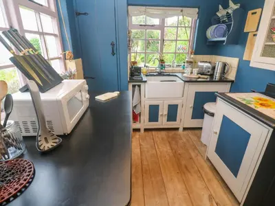 a kitchen with blue walls and a black counter top at Mermaid Cottage in Helston