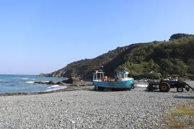 a boat and a tractor on a rocky beach at Mermaid Cottage in Helston