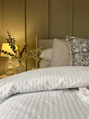 a bed with a white comforter and a table with a lamp at SeaNest, Aggie Home by the sea in St. Agnes