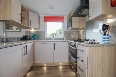 a kitchen with white cabinets and a sink and a window at The Maples, no 56 in St Austell