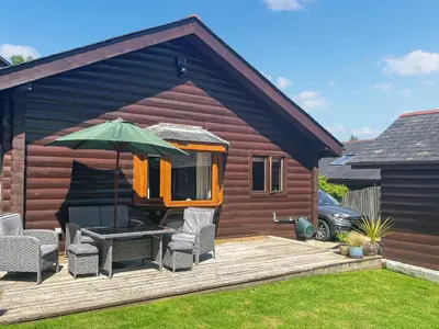 a house with a deck with chairs and an umbrella at Maple Leaf Cottage in Padstow