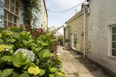 an alley in an old town with flowers at Bessie Ellens Cottage - 1 Pet Welcome - Central Location - Free WiFi in Fowey