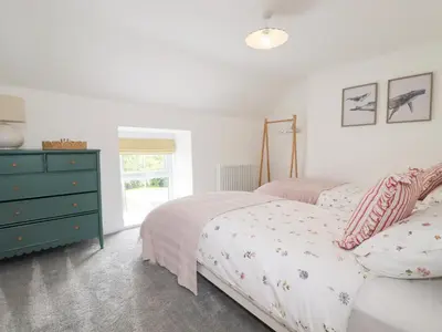 a white bedroom with two beds and a dresser at Glendale in Port Isaac