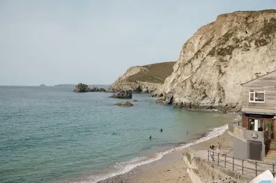 a beach with a house and people in the water at Luxury Cornish Cottage & Modern Cabin with Garden, Central St Agnes in St. Agnes