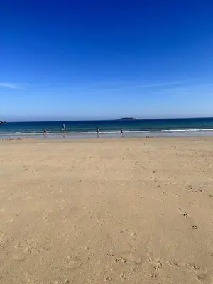 a beach with people walking on the sand and the ocean at Headlands- Stylish Oceanfront Property on Harlyn Bay in Padstow