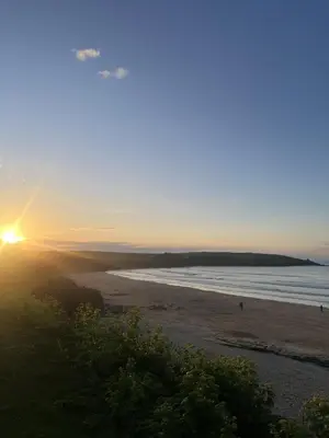 a sunset on a beach with the sun setting at Headlands- Stylish Oceanfront Property on Harlyn Bay in Padstow