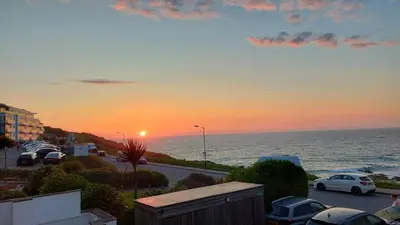 a sunset over the ocean with cars parked in a parking lot at 4 Fistral Beach Apartments, Newquay, TR7 1FR in Crantock