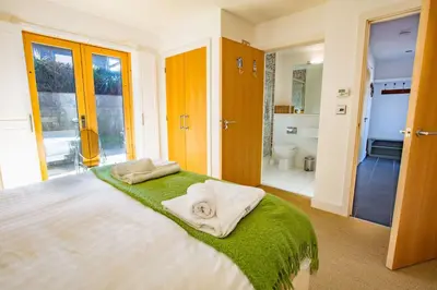 a bedroom with a bed with a green blanket and a bathroom at House 28 in Looe