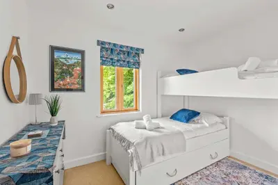 a white bedroom with a bunk bed and a desk at House 25 in Looe