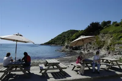 a group of people sitting at picnic tables on the beach at House 25 in Looe
