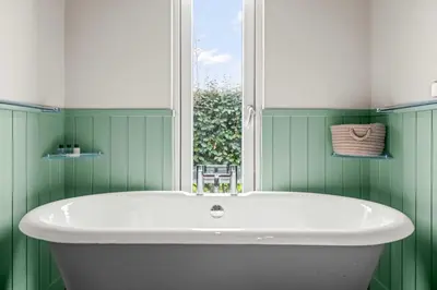 a bath tub in a green bathroom with a window at House 39 in Looe