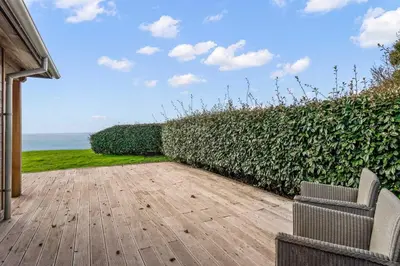 a patio with a hedge and a chair and the ocean at House 39 in Looe