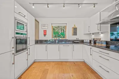 a kitchen with white cabinets and a wooden floor at House 4 in Looe