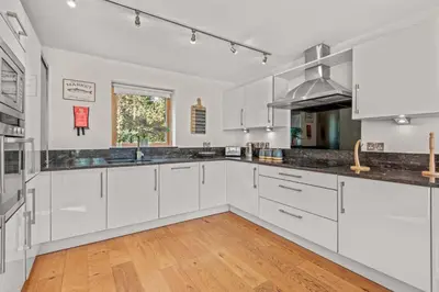 a kitchen with white cabinets and a wooden floor at House 4 in Looe