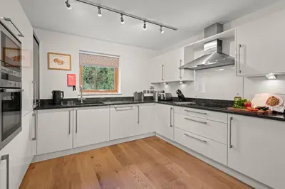 a kitchen with white cabinets and a wooden floor at House 5 in Looe