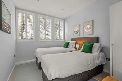 two beds in a bedroom with white walls and windows at House 46 in Looe