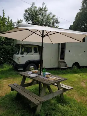 a picnic table with an umbrella in front of a truck at Monroe Horsebox Glamping in Porthleven