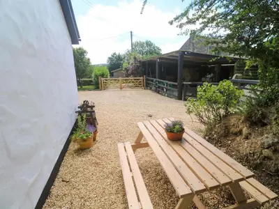 a wooden bench next to a building with two potted plants at Lavender Cottage in Helston
