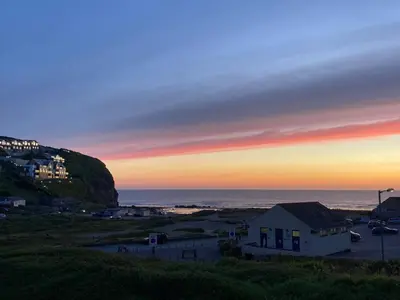 a sunset over a beach with a house and the ocean at 'The Dunes', Porthtowan in Porthtowan