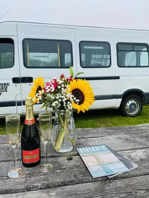 a table with flowers and a bottle of wine and glasses at Quiet peaceful relaxing off grid Campervan Seaview and Ponies in Carbis Bay