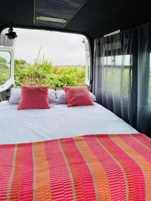 a bed in the back of a van with red pillows at Quiet peaceful relaxing off grid Campervan Seaview and Ponies in Carbis Bay