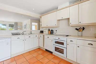 a kitchen with white cabinets and an orange tile floor at Chough at Highcliffe in Polzeath