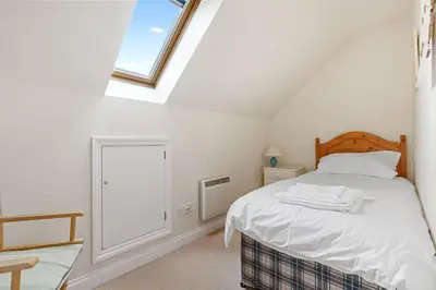 a white bedroom with a bed and a window at Chough at Highcliffe in Polzeath