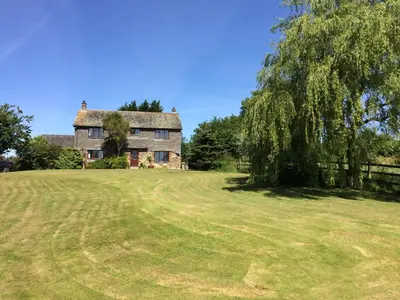 an old house in a field with a tree at Trecorme Barton in Quethiock