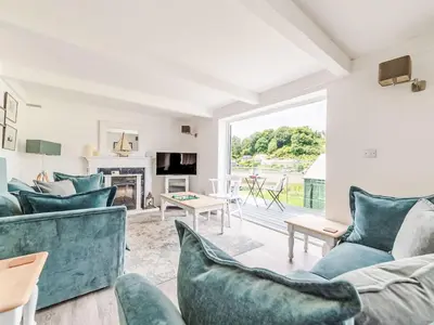 a living room with blue furniture and a large window at Holiday Home Riverside Cottage by Interhome in Lerryn