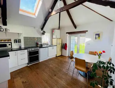 a kitchen with white cabinets and a table with chairs at Cleave Cottage in Crackington Haven
